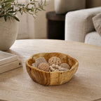 Cove Chalet Teak Wavy Bowl Small in natural wood filled with decorative woven balls, beads and textured accents on a coffee table.