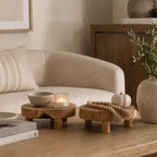 Cove Chalet Teak Tray Set of 2 in natural wood displayed on a coffee table with a candle, ceramic bowl, decorative beads and a small pumpkin.