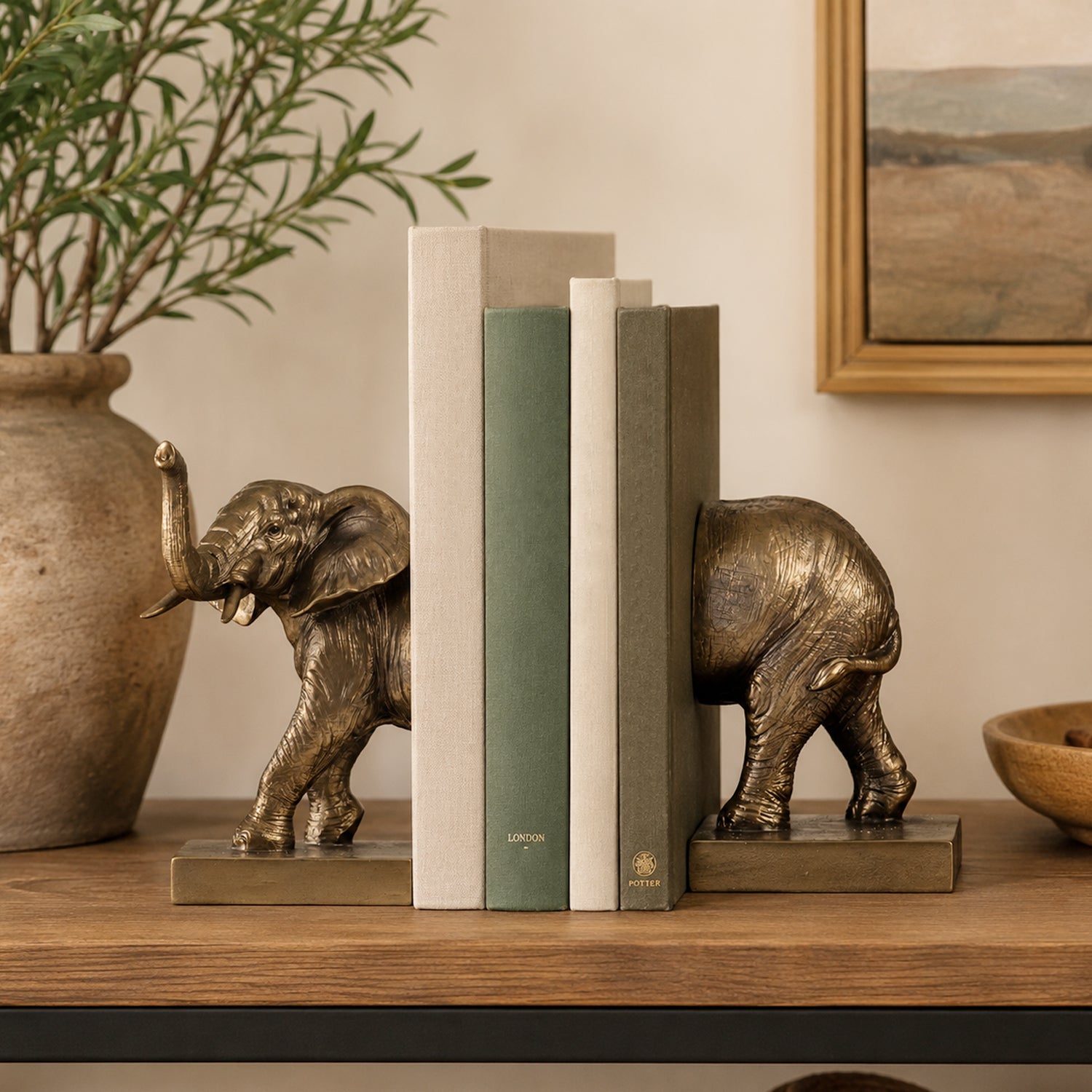 Design Republique Elephant Bookends in bronze displayed on a wooden console with neutral books and decorative foliage.
