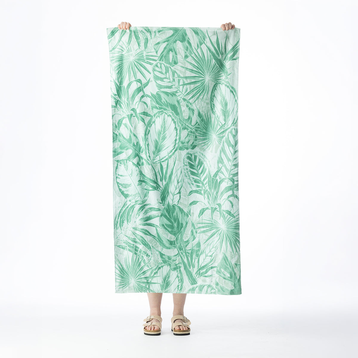 Mint green beach towel featuring an all-over tropical leaf print, held up against a white background.