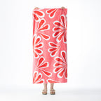 Pink-red Seaside Supplies beach towel featuring a bold all-over white floral design, held up against a white background.