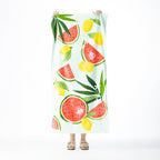 Light mint Seaside Supplies beach towel featuring a colourful watermelon, lemon and tropical leaf design, held up against a white background.