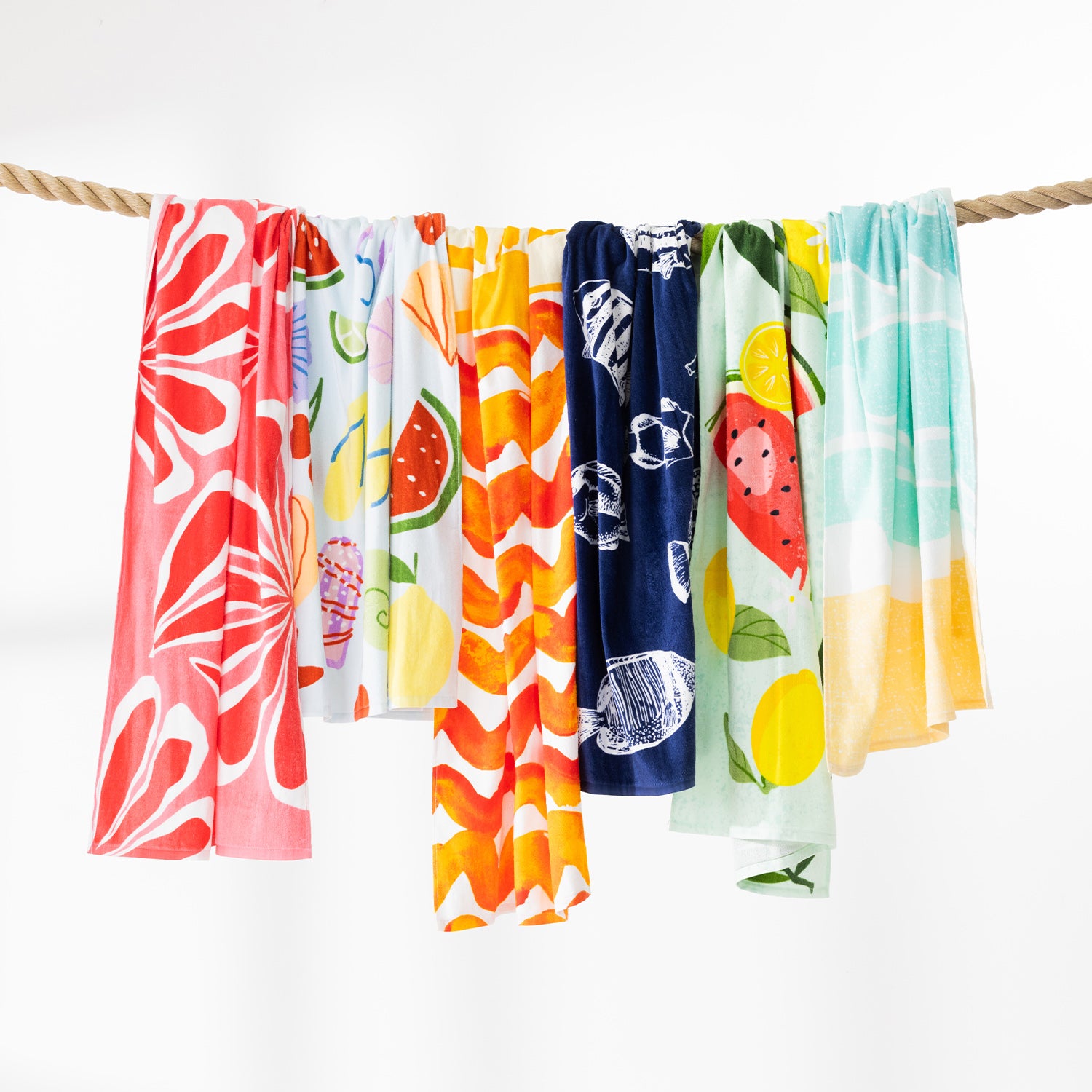 Assorted Seaside Supplies beach towels in bright summer prints hanging side by side over a rope.