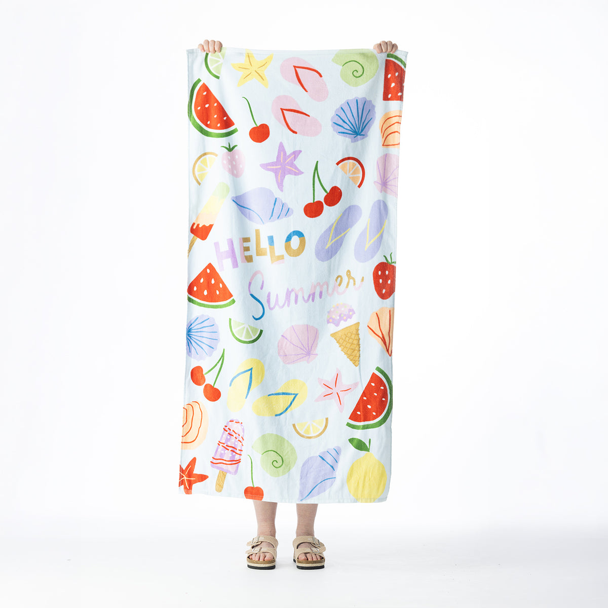 Light blue Seaside Supplies beach towel featuring colourful summer icons and a “Hello Summer” design, held up against a white background.