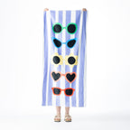 Blue and white striped Seaside Supplies beach towel featuring five colourful sunglasses designs, held up against a white background.
