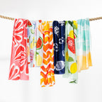 Assorted Seaside Supplies beach towels in bright summer prints hanging side by side over a rope.