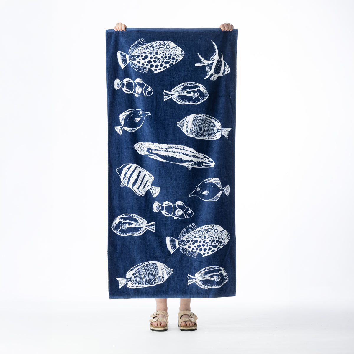 Navy Seaside Supplies beach towel featuring an all-over white illustrated fish design, held up against a white background.