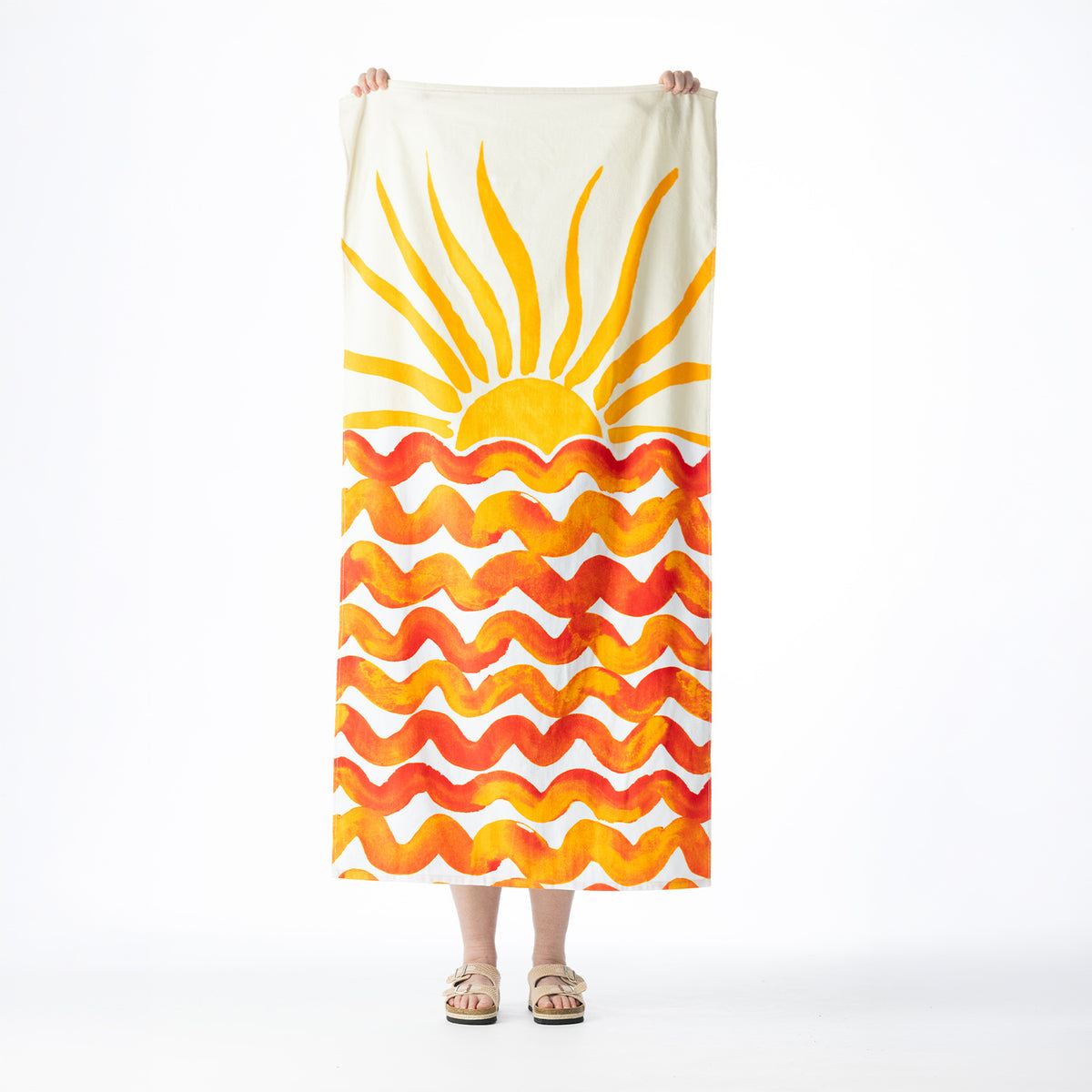 White Seaside Supplies beach towel featuring a bold yellow sunburst and orange wavy ocean design, held up against a white background.