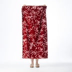 Deep red Seaside Supplies beach towel featuring an all-over pale pink bow and ribbon design, held up against a white background.