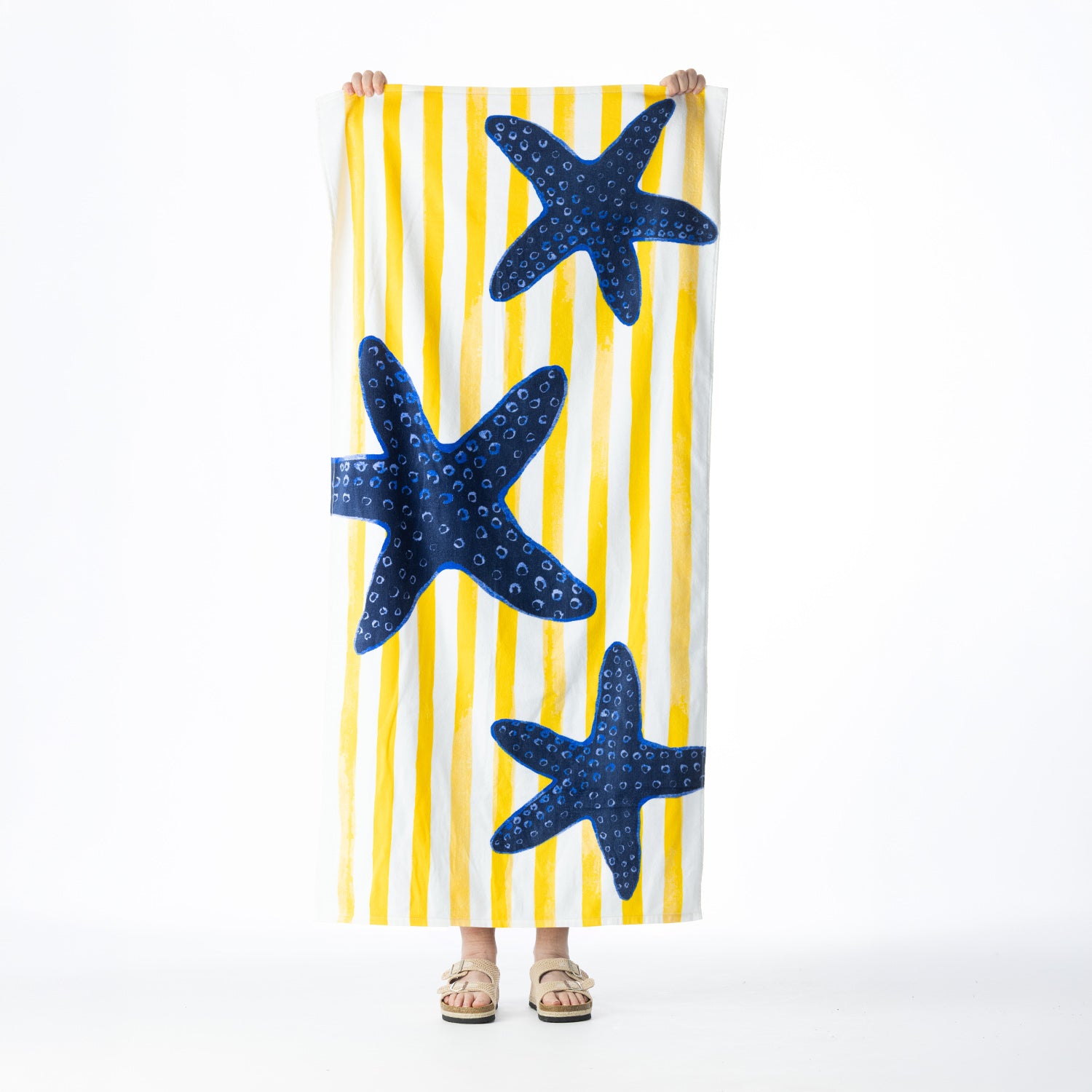 Yellow and white striped Seaside Supplies beach towel featuring three large navy blue starfish, held up against a white background.