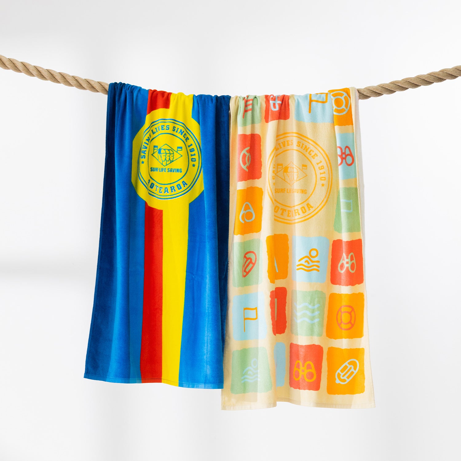 Surf Life Saving beach towels displayed over a rope, including the blue striped design and a colourful beach-themed print.