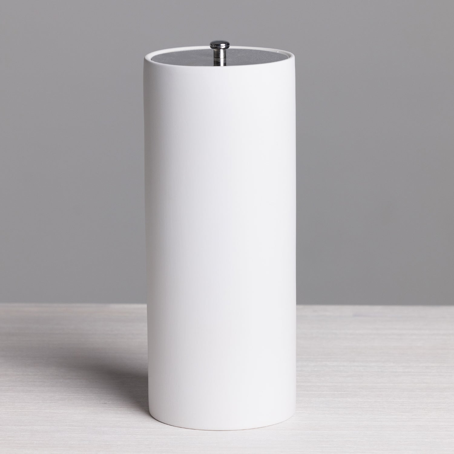 A sleek white freestanding toilet roll holder with a minimalist cylindrical design and brushed metal top detail provides stylish, convenient bathroom storage.
