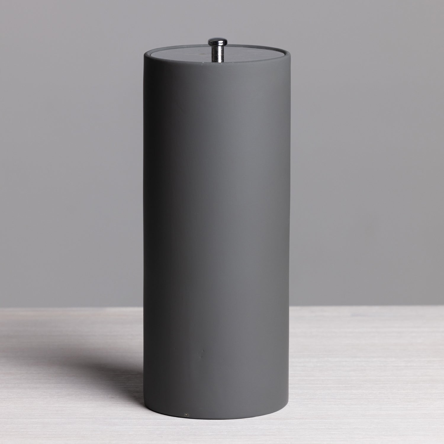 A sleek charcoal freestanding toilet roll holder with a minimalist cylindrical design and brushed metal top detail provides stylish, convenient bathroom storage.