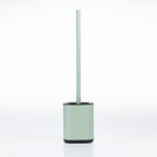 A minimalist toilet brush with a pale sage green handle and base, accented by a black rim and bottom base, set against a seamless white background.