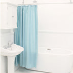 Light blue shower curtain hanging beside a white bathtub and sink in a bright bathroom.