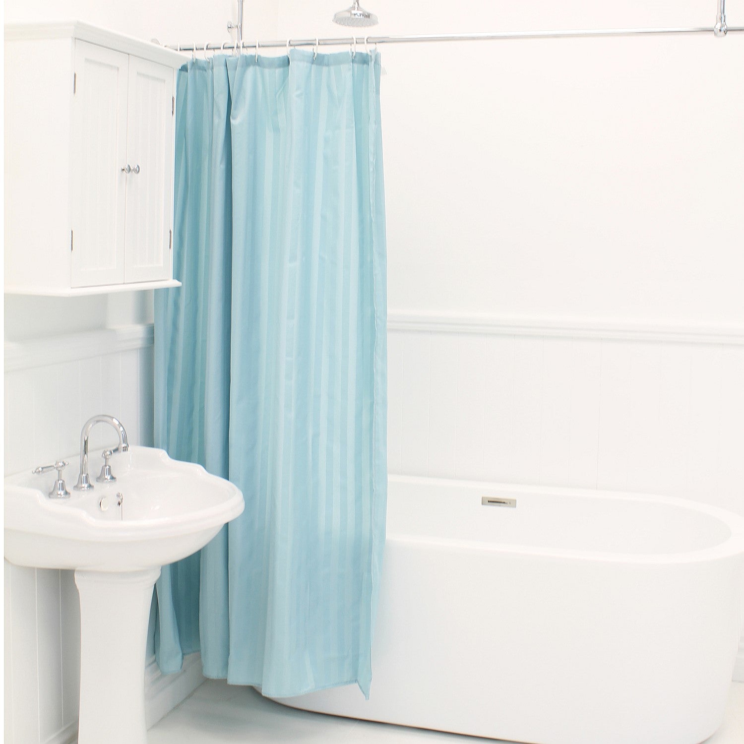 Light blue shower curtain hanging beside a white bathtub and sink in a bright bathroom.