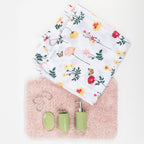 Five-piece bathroom set including a white floral shower curtain, blush pink bathmat, sage green soap dispenser, tumbler, soap dish, and silver shower rings, arranged on a white background.