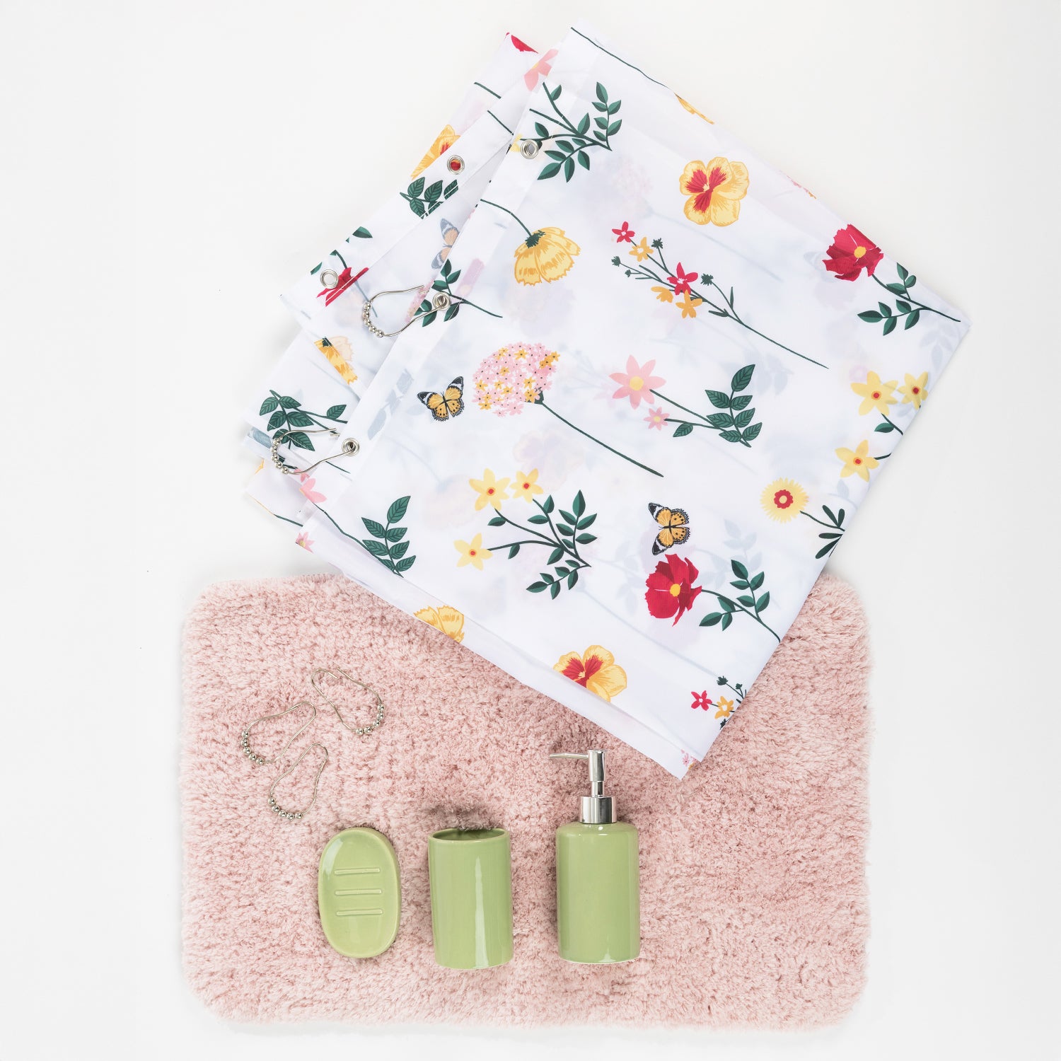 Five-piece bathroom set including a white floral shower curtain, blush pink bathmat, sage green soap dispenser, tumbler, soap dish, and silver shower rings, arranged on a white background.