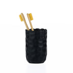 A matte black textured tumbler with a softly scalloped rim, styled with two bamboo toothbrushes.