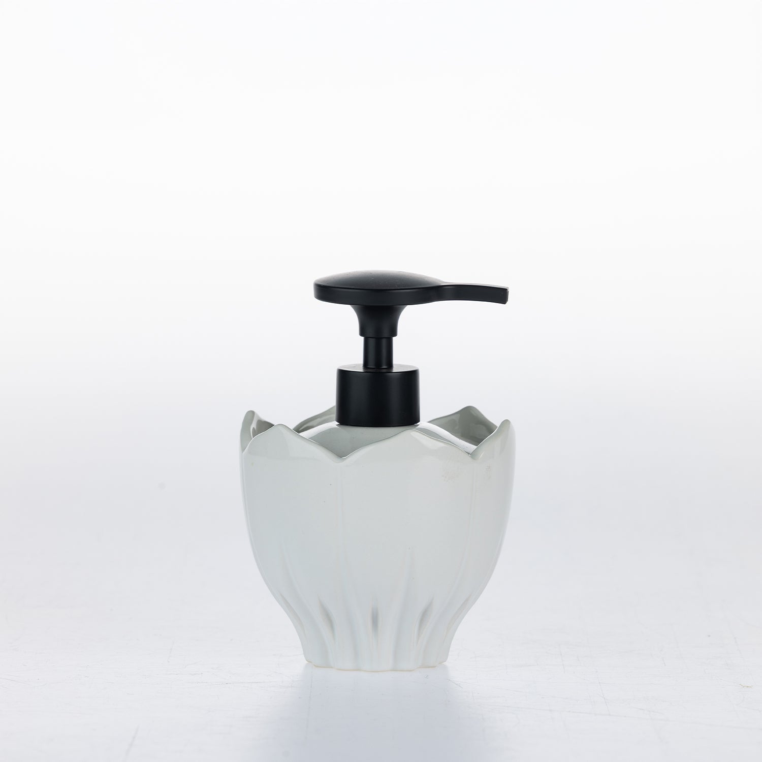 A white ceramic soap dispenser with a black pump, shaped like a lotus flower, on a white background.
