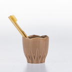 A Natural ceramic toothbrush holder with a bamboo toothbrush resting inside, set against a clean white background.