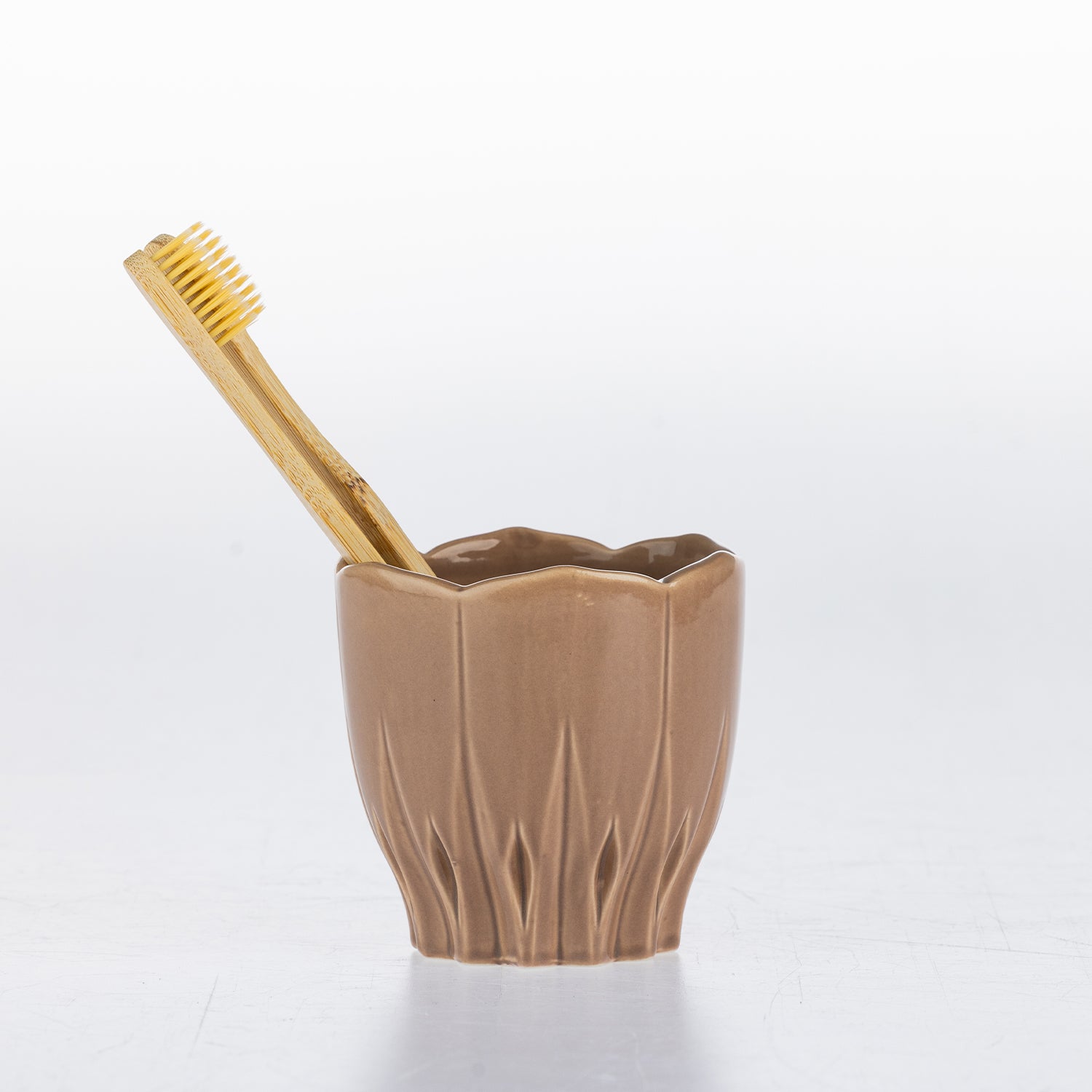 A Natural ceramic toothbrush holder with a bamboo toothbrush resting inside, set against a clean white background.