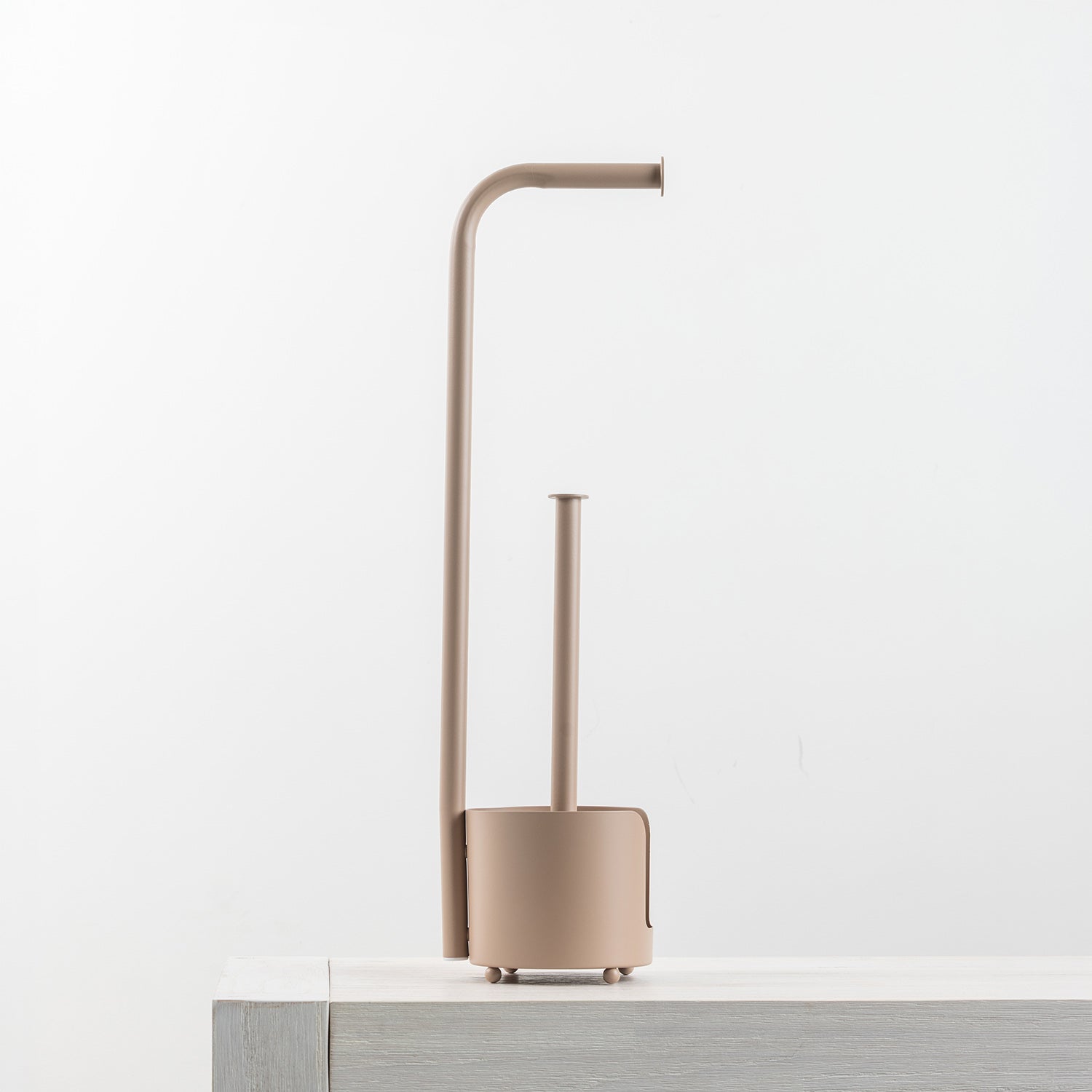A minimalist toilet paper holder with a matching holder and a curved, modern design in a warm taupe-beige color, shown on a light gray surface against a white background.