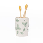 Ceramic Gracious Living Irina Floral Toothbrush Holder in Ivory with a soft green floral pattern, holding two natural bamboo toothbrushes.