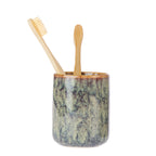 Design Republique Clara Fade Tumbler in Green, featuring a cylindrical ceramic design with a mottled green and grey glazed finish, holding two bamboo toothbrushes.