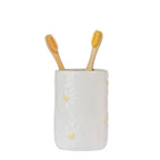 Marlo Daisy Ceramic Tumbler in Ivory, featuring a glossy ceramic finish with raised white daisy flowers and soft yellow centres, displayed with two bamboo toothbrushes.