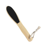 A wooden foot scrubber with a black textured scrubbing pad on one end and a white rope loop at the handle's end, shown on a plain white background.