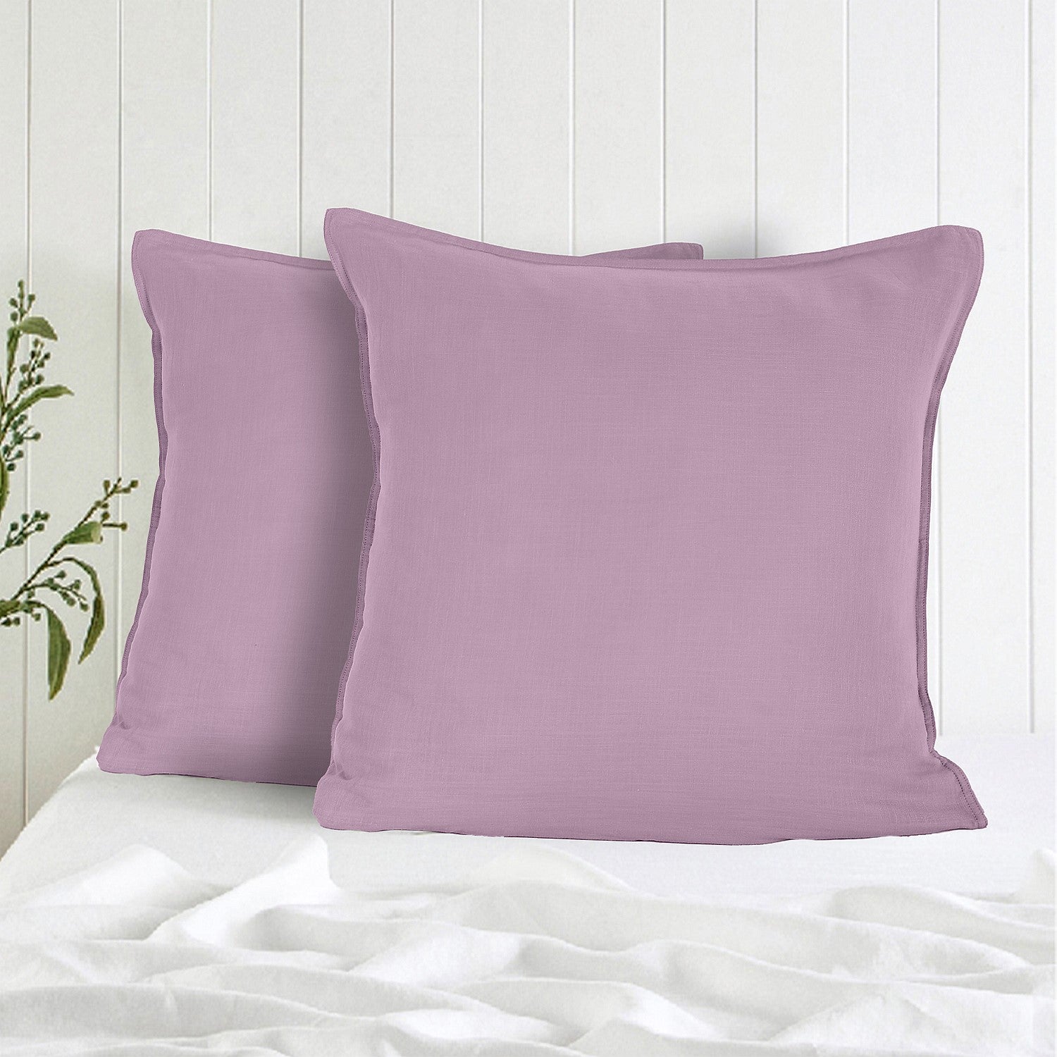 Two purple pillows on a white bed with a light wooden headboard.