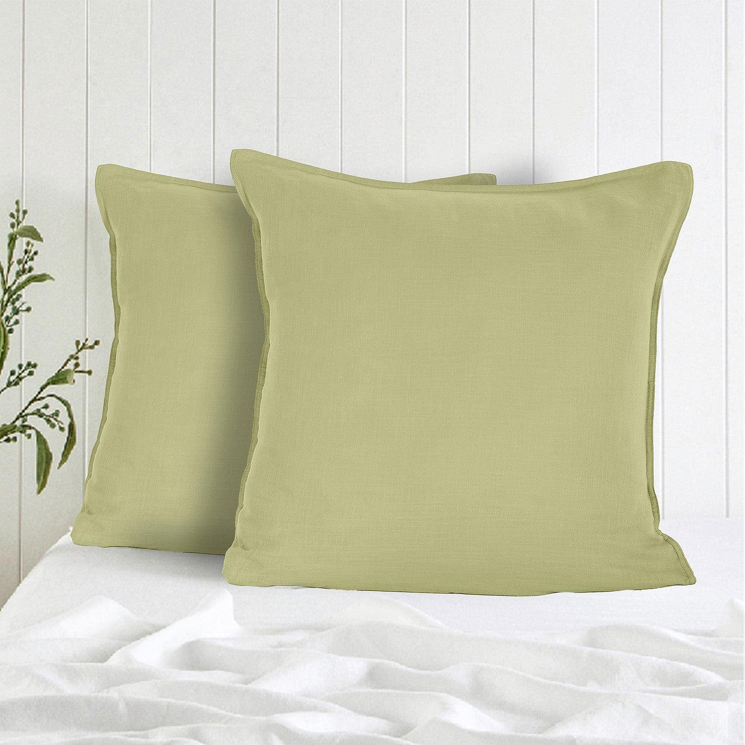 Two green pillows on a bed with a white wooden panel background