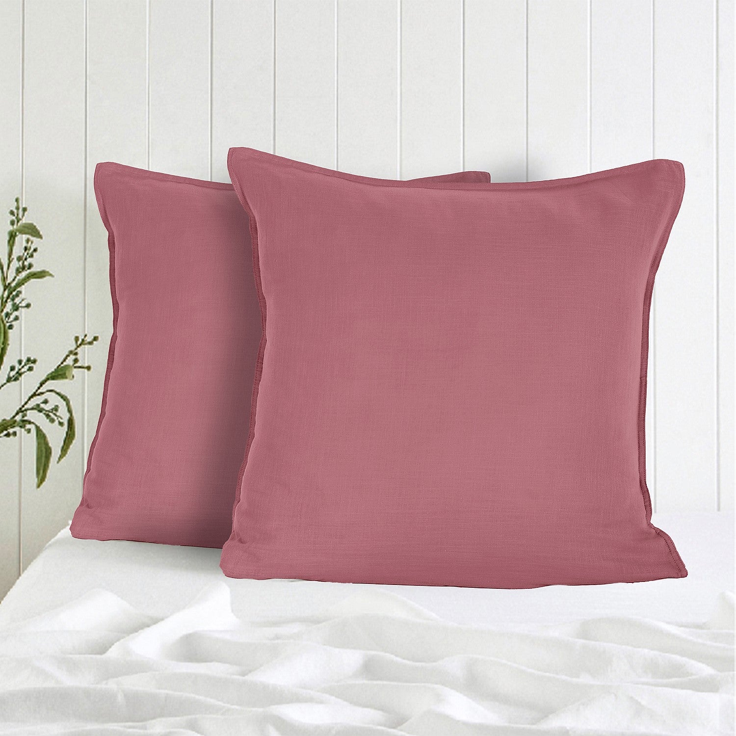 Two pink pillows on a white bed with a light wooden headboard.