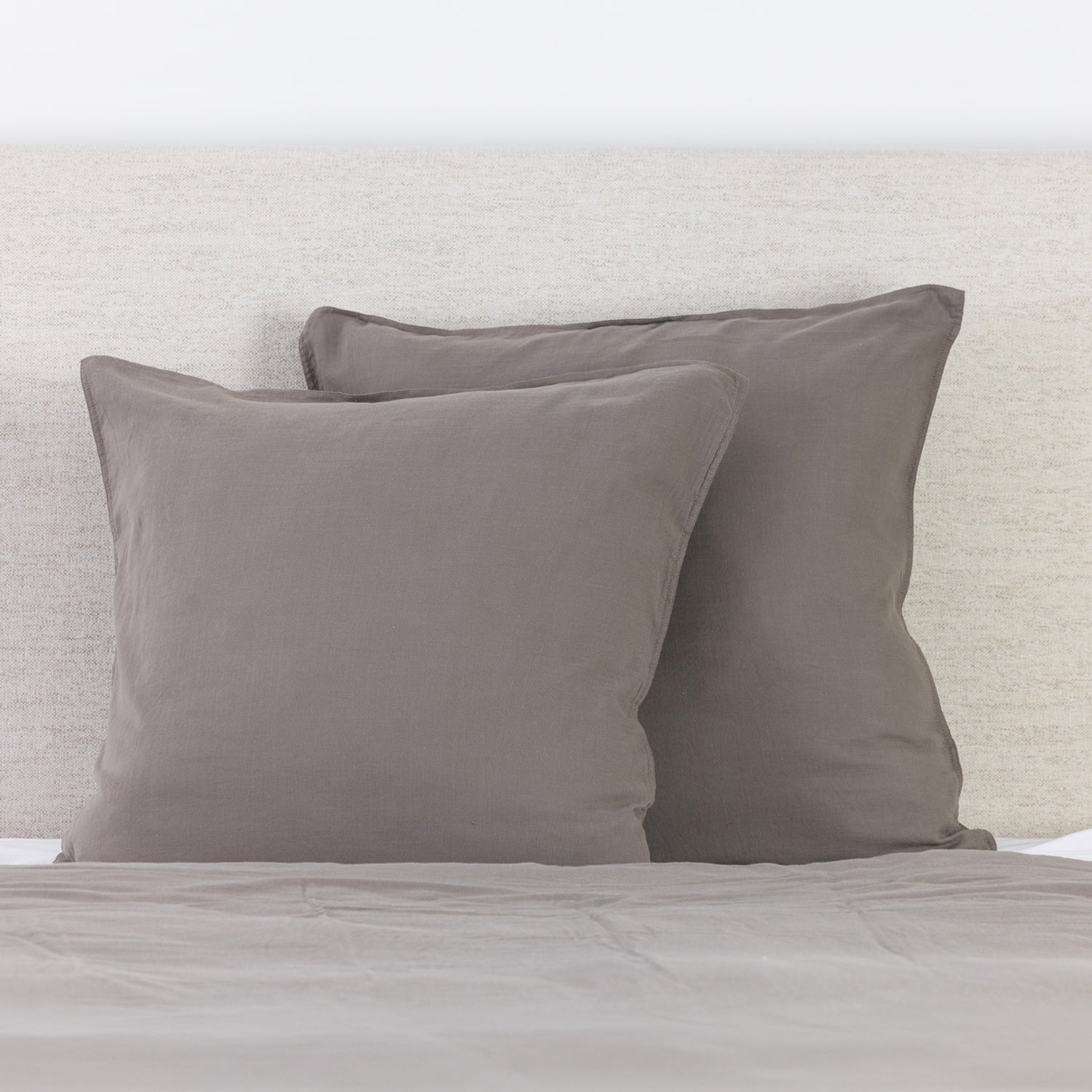 Med brown linen look European pillowcases styled on a bed with a neutral fabric headboard.