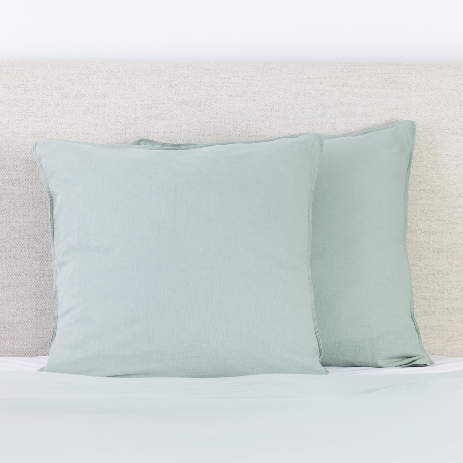 Sage linen look European pillowcases styled on a bed with a neutral fabric headboard.
