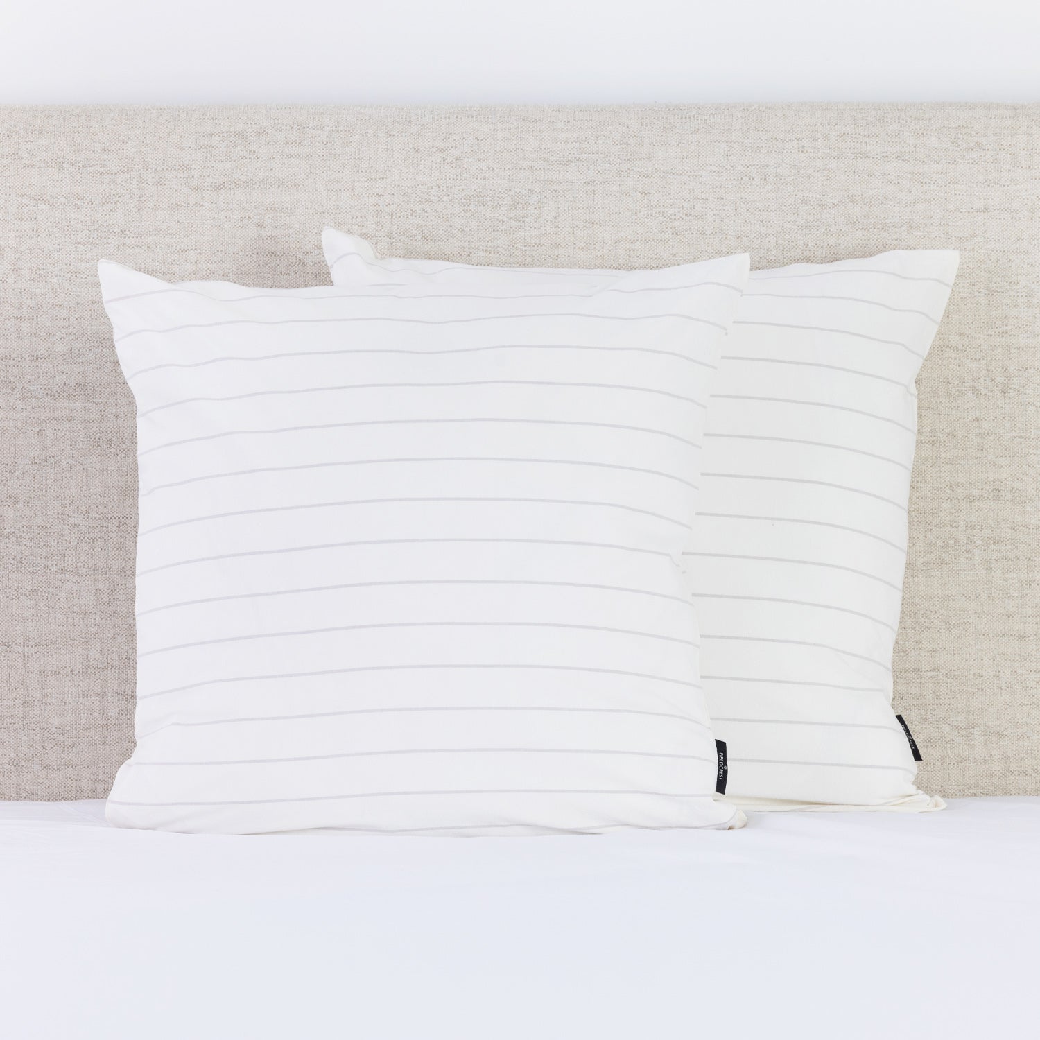 A pair of crisp white pinstripe European pillowcases brings a fresh, timeless look to a neatly styled bed.