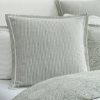 A square decorative throw pillow with vertical gray and white stripes, styled on a bed with matching patterned bedding and pillows.
