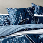 Close-up of the Logan & Mason Willa 100% Cotton Duvet Cover Set in Blue, showcasing the navy botanical print with large floral motifs and a contrasting light blue striped reverse.