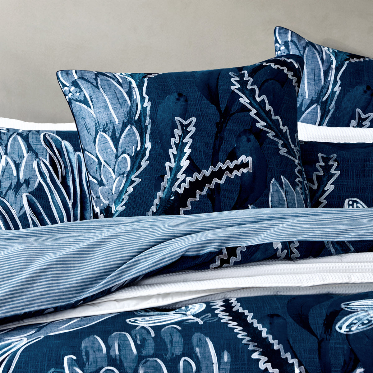Close-up of the Logan & Mason Willa 100% Cotton Duvet Cover Set in Blue, showcasing the navy botanical print with large floral motifs and a contrasting light blue striped reverse.
