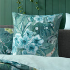Logan & Mason Lila Surf European Pillowcase in Green styled on a bed with coordinating tropical bedding, charcoal cushions and a pale blue striped duvet reverse.
