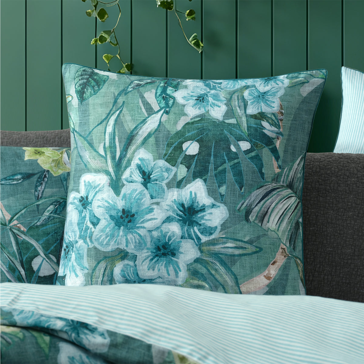 Logan & Mason Lila Surf European Pillowcase in Green styled on a bed with coordinating tropical bedding, charcoal cushions and a pale blue striped duvet reverse.