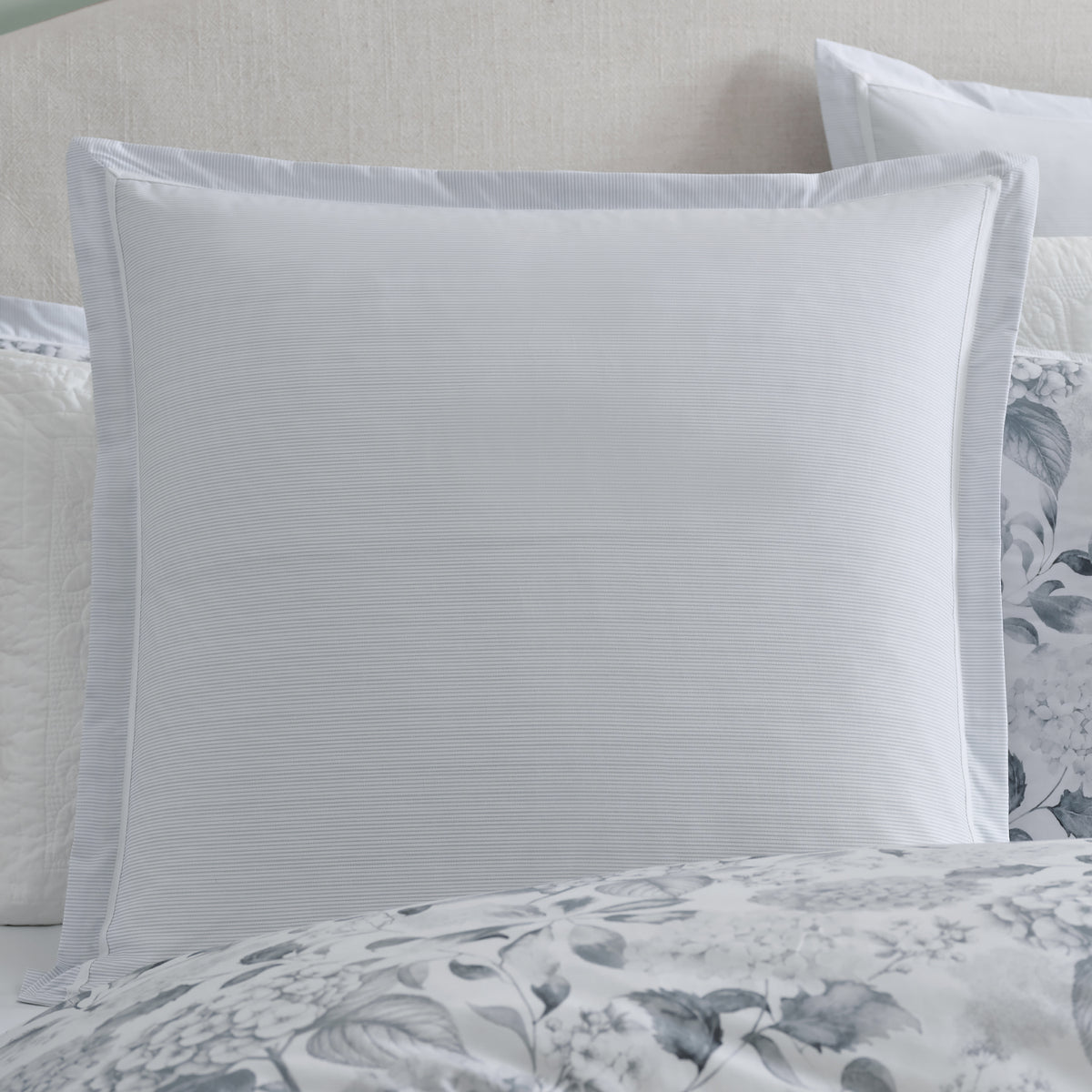 Styled view of the Private Collection Hydrangea 100% Cotton Euro Pillowcase on a bed, showcasing its subtle grey and white stripe design alongside coordinating floral bedding.
