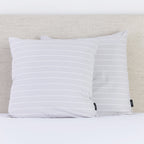A pair of Mist grey European pillowcases with subtle white pinstripes brings a refined, contemporary touch to a neatly styled bed.
