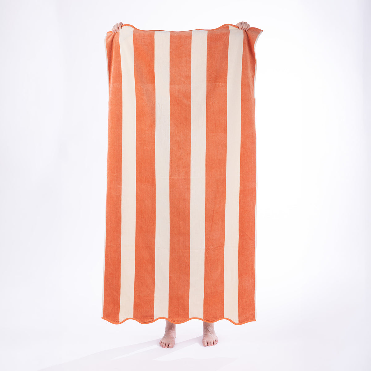 Model holding a Coral and cream striped Cove Maldives Beach Towel against a white studio background.