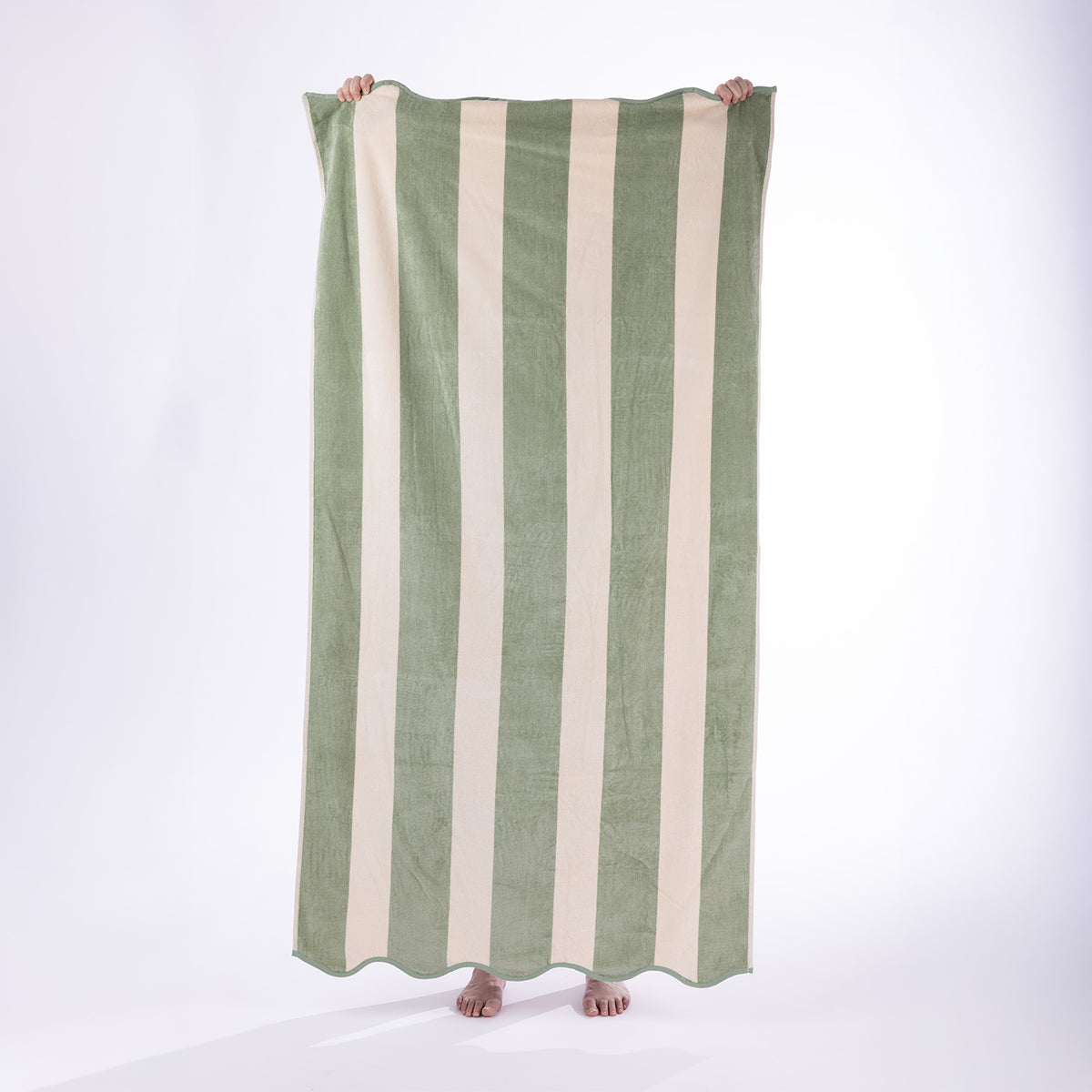 Model holding a green and cream striped Cove Maldives Beach Towel against a white studio background.