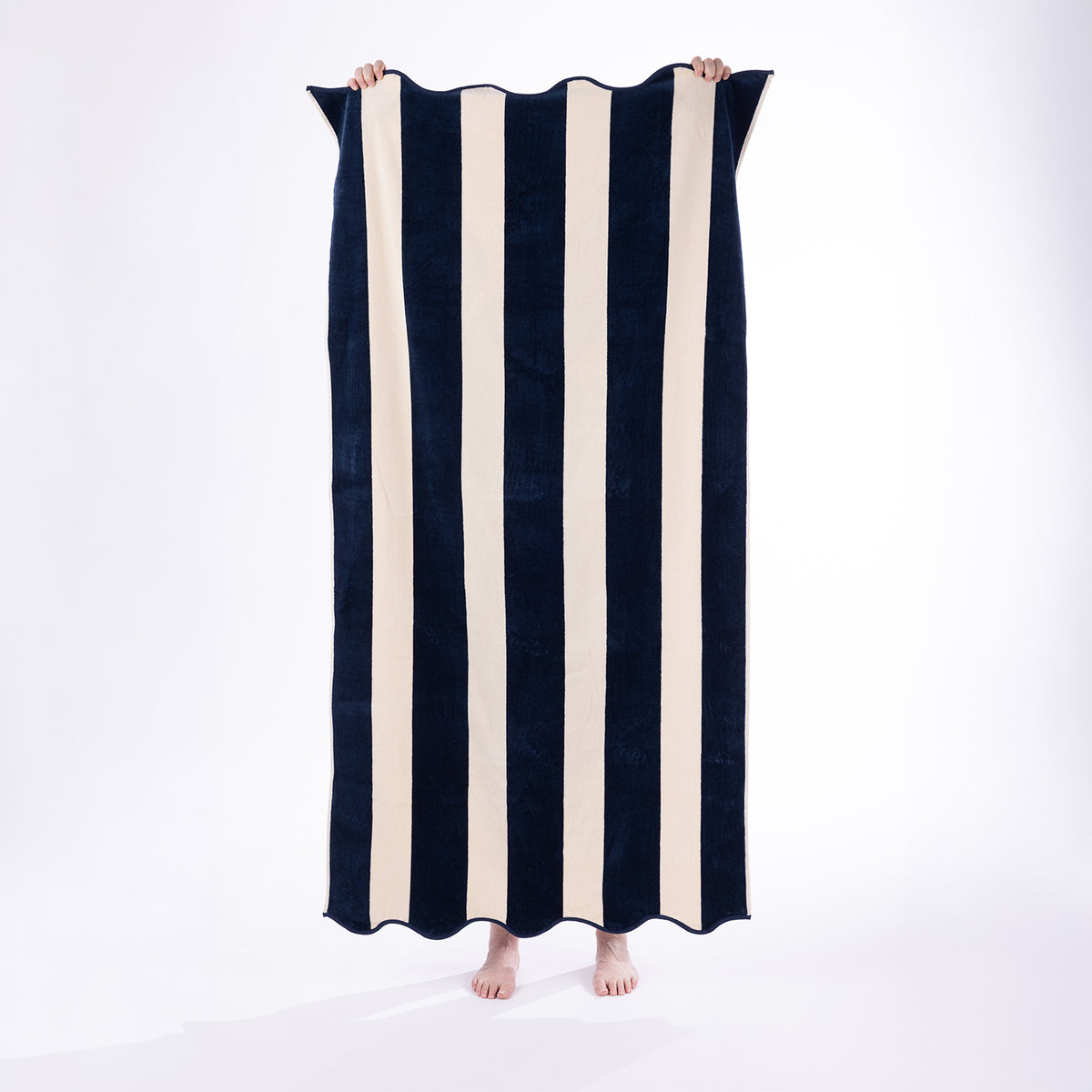 Model holding a navy and cream striped Cove Maldives Beach Towel against a white studio background.