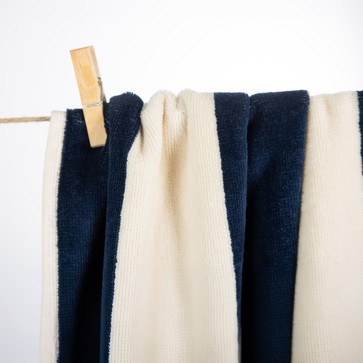 A close-up of striped towels hanging from a wooden clothespin on a thin line against a plain white background.