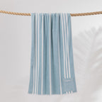 Cove Pocket Towel in Seafoam Blue with white vertical stripes, hanging over a rope with a convenient zippered pocket at the bottom.
