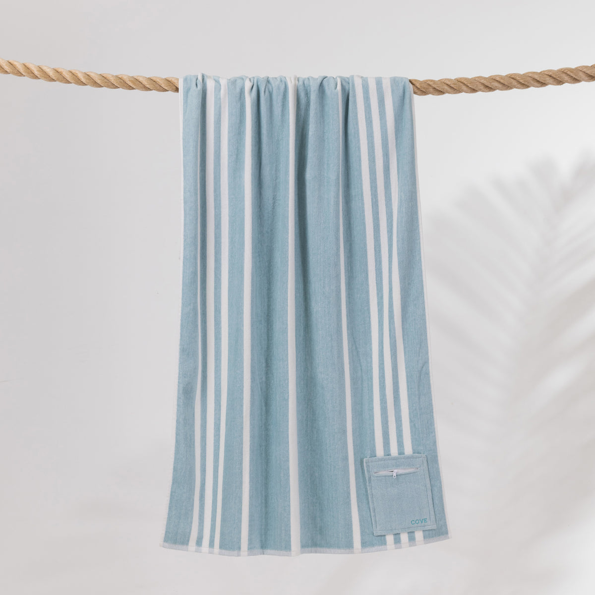 Cove Pocket Towel in Seafoam Blue with white vertical stripes, hanging over a rope with a convenient zippered pocket at the bottom.